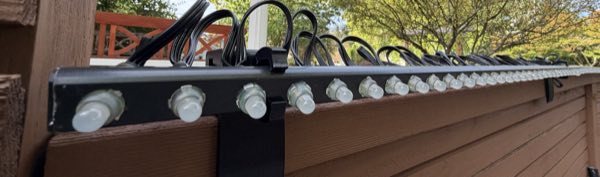 A bar of large pixel nodes mounted along the top of the fence with wiring behind it