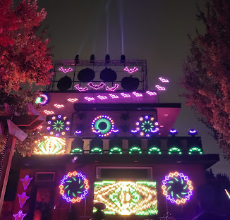 Halloween display with bats along the roofline and spotlight beams in the sky