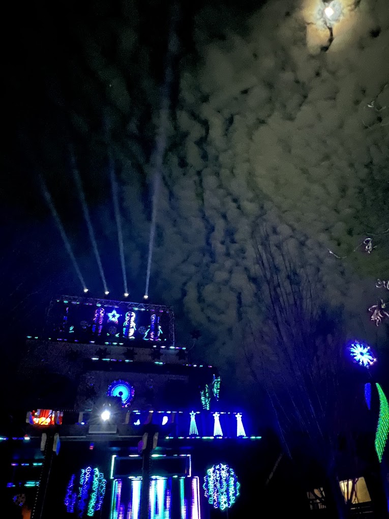Spotlight beams rising from the Christmas display into a cloudy moonlit sky